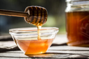 Honey dripping off a honey spoon into a glass bowl