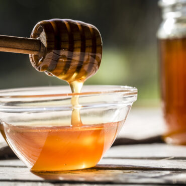 Honey dripping off a honey spoon into a glass bowl